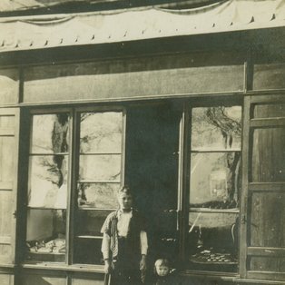 Mercerie Courdesses 1925 Situé à l'endroit de la boulangerie Voinot Valérie Courdesses, mère de Jacqueline épouse Rascol, et son fils Emile. En plus de la Mercerie, elle vendait des chaussures. MERCERIE COURDESSES Photo d'un groupe de personne devant un commerce ancien
