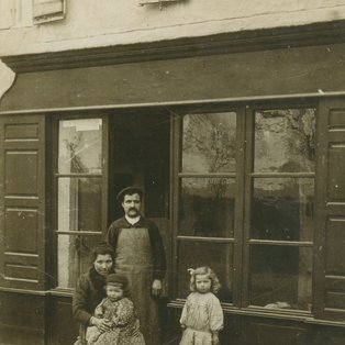 1910 Le cordonnier Vaissières était appelé, le cordonnier Pistou. La petite fille à droite s'appelait Emilie. Elle épousera Elie Tissendié, les diligences Photo du cordonier et les enfants devant le commerce