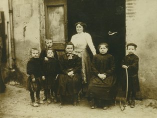Devant l'atelier du Maréchal-ferrant, de gauche à droite : Emile Tissandié et son frère Elie, Fauvel, Marthe Arnald (mère de Jeannette Miquel), Léa Baldi, Jeanne et Eloi Gleize Photo d'un groupe de personne devant un commerce