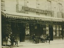 Grand café de l'univers, au centre M. Bréchand assis, un sac sur les genoux avec deux autres personnes. Tout le monde porte des sabots. Le café a ensuite été vendu à M. Gaussière Photo d'un groupe de personnes devant le grand café de l'univers